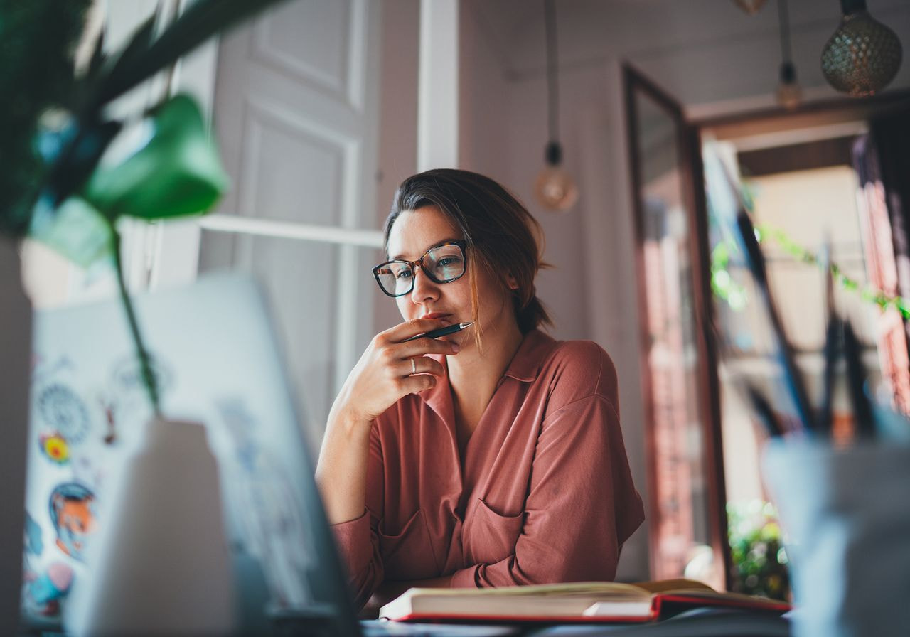A woman in glasses is sitting at a desk and reading about brand awareness strategies from a laptop.